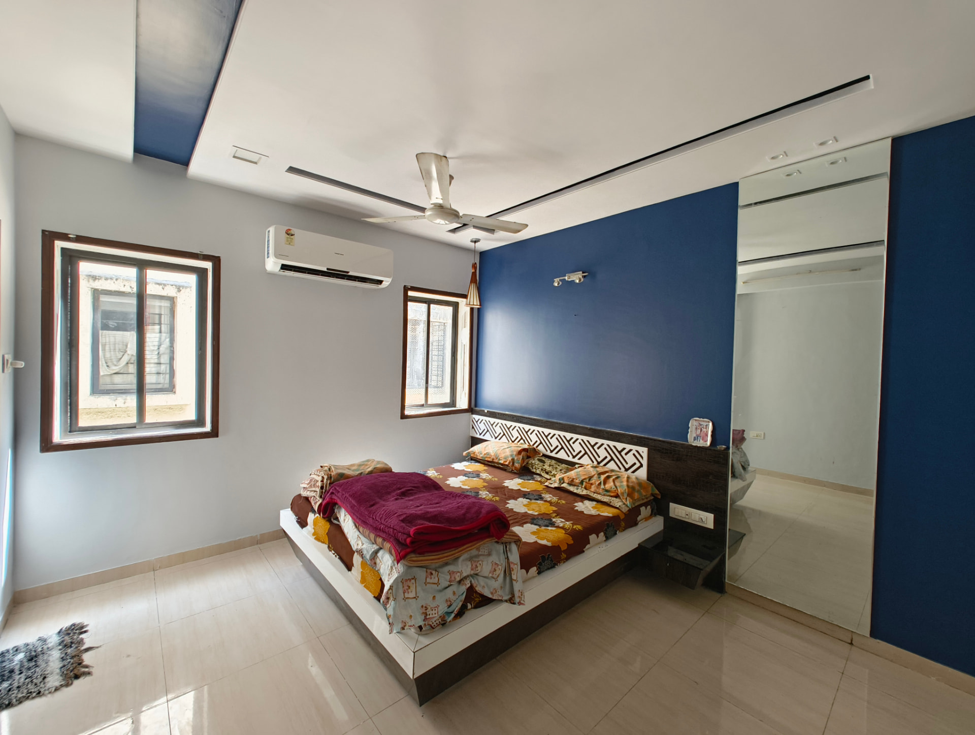 Bedroom interior with a deep blue accent wall, full-height mirror panel and a carved white patterned headboard