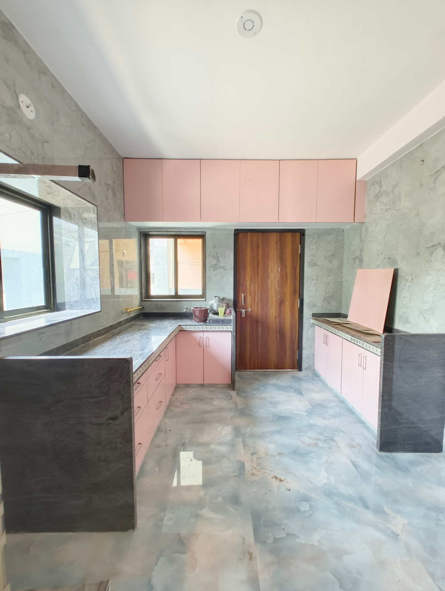 Modular kitchen in progress with blush pink cabinetry, grey marble-effect wall tiles and dark stone countertops