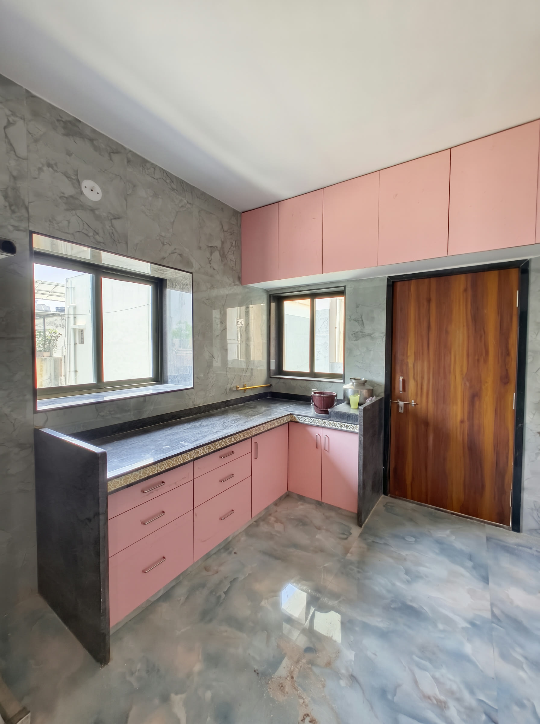 L-shaped modular kitchen design in Surat with blush cabinetry, dark countertop and marble-look splashback